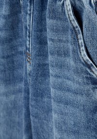Tessuto di denim azzurro chiaro, con una superficie leggermente testurizzata, cuciture visibili in un arancio contrastante e un dettaglio della tasca.