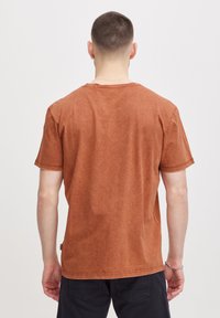 Camiseta de algodón de color óxido con un corte relajado, mangas cortas y escote redondo. Presenta una textura sutil y costuras mínimas.