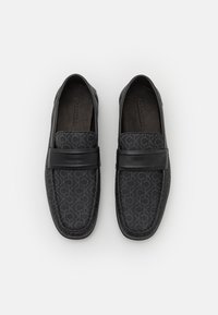 Mocassins noirs avec une tige texturée arborant un motif logo répétitif et une bande en cuir lisse sur le devant. Semelle intérieure rembourrée.