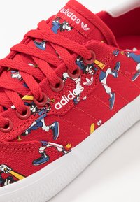 Rote Leinensneaker mit weißer Gummisohle. Buntes Cartoon-Muster und rote Schnürsenkel. Adidas-Logo auf der Zunge und an der Seite.