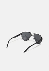 Ochelari de soare aviator negri cu lentile gri, cadru metalic, formă curbată și brațe negre elegante. Include perne pentru nas pentru confort și aderență.