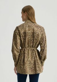 Bruine en beige blouse met een luipaardprint, gemaakt van lichtgewicht stof. Heeft een ceintuur in de taille en lange, opgeblazen mouwen.