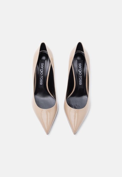Μπεζ γυαλιστερά ψηλοτάκουνα παπούτσια μυτερά στη μύτη με μαύρα εσωτερικά πέλματα με την ετικέτα «sergio rossi», από πάνω, σε απλό φόντο.