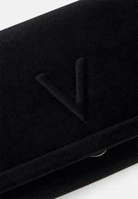 Svart sammetsplånbok med en upphöjd "V"-logotyp. Ytan är mjuk, med en smidig stängning och subtil sömdekor.