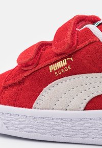 Piros nubuk sneakers fehér gumitalppal, tépőzáras pántokkal és arany Puma logó díszítéssel.