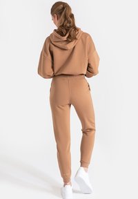 Brązowa bluza z kapturem w parze z dopasowanymi dresami. Miękka tekstura, luźny krój, elastyczny pas. Uzupełnione białymi sneakersami.