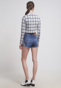 Top gris a cuadros recortado con mangas largas combinado con shorts de mezclilla azul. Botines blancos con detalles en negro completan el conjunto.