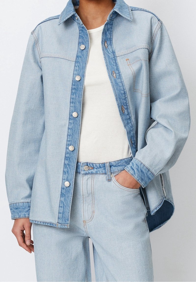 Vaaleansininen farkkupaita, jossa on napitettava etuosa, rintatasku ja erottuva sininen kaulus. Yhdistetty vaaleansinisiin farkkuleggingseihin.