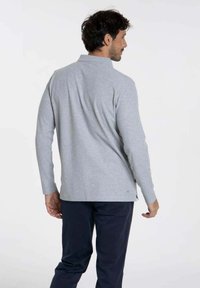 Polo gris à manches longues avec col, présentant des fentes latérales à l'ourlet, assorti à un pantalon sombre. Texture douce et coupe ajustée.