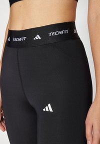 Zwarte Techfit-legging met een brede elastische tailleband met witte branding. Glad, rekbaar materiaal met een aansluitend ontwerp. Witte logodetail.