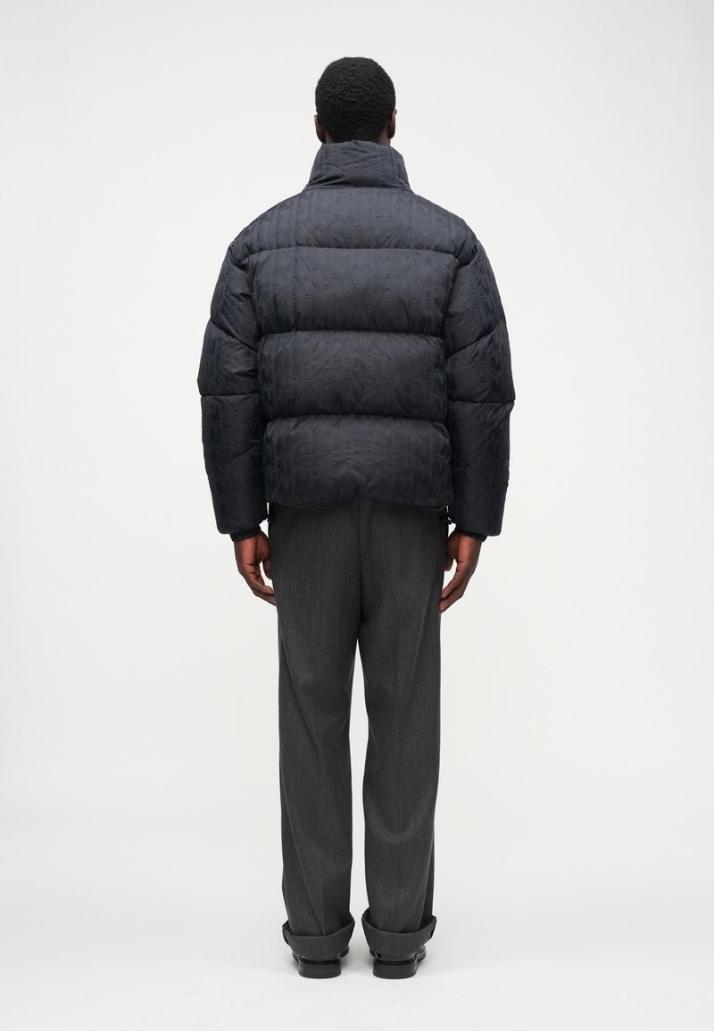 Puffer jacket in dark navy, featuring quilted design and high collar. Paired with gray trousers, showcasing a relaxed fit and rolled cuffs.