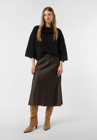 Oversized black knit sweater with a cowl neck, paired with a flowing brown satin skirt and tan suede pointed-toe boots.