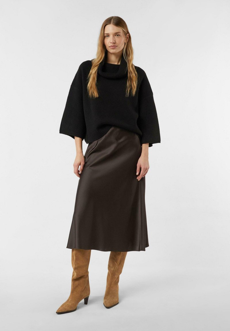 Oversized black knit sweater with a cowl neck, paired with a flowing brown satin skirt and tan suede pointed-toe boots.