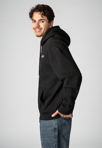 Black pullover hoodie with a drawstring, front pocket, and ribbed cuffs. Soft fabric texture, paired with blue denim jeans.