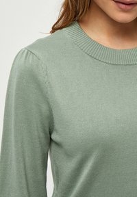 Maglione a coste di un verde chiaro, con scollo rotondo e maniche leggermente a sbuffo. Tessuto morbido, offre una silhouette attillata.