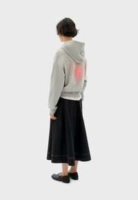 Sudadera gris recortada con un gráfico de sol rosa en la parte posterior, combinada con una falda negra a la altura de la rodilla con costuras blancas y zapatos negros tipo slip-on.