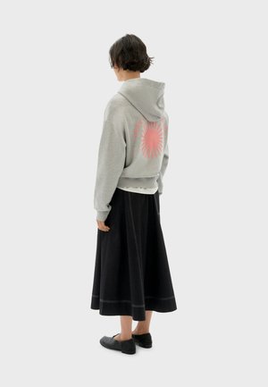 Grijze cropped hoodie met een roze zon grafiek op de achterkant, gecombineerd met een zwarte knie-lange rok met witte stiksel, en zwarte instapschoenen.