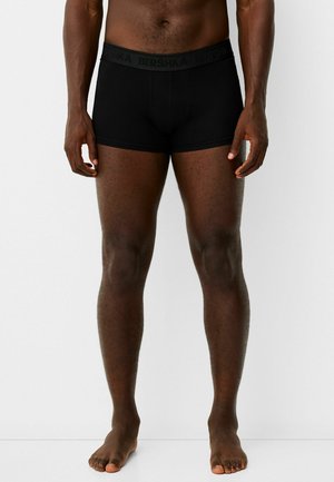 Schwarze Boxer-Shorts mit einem weichen Bund, der das "BERSHKA"-Logo trägt. Der Stoff ist glatt und eng anliegend, mit einer Länge bis zur Mitte des Oberschenkels und ohne sichtbare Muster.