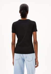 Sort ribbet t-shirt med korte ærmer, der har en tætsiddende halsudskæring, parret med lyseblå afslappede jeans. Bagansigt.