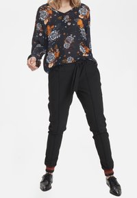 Blouse à manches longues navy fleuri avec des motifs orange et blancs, associée à un pantalon noir fuselé et des chaussures noires avec des accents rouges.
