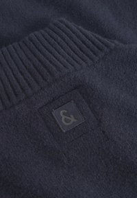 Marineblauer Wollpullover mit einem gerippten Kragen und einem rechteckigen Logo-Patch mit einem schwarzen Ampersand-Symbol. Weicher Stoff und nahtloses Design.