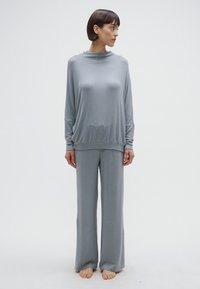 Világosszürke, hosszú ujjú, laza szabású felső magas nyakkal, hozzáillő bő szárú nadrággal, puha, sima anyagból készült.