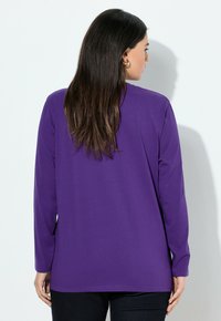 Lange mouwen paarse T-shirt van een zachte stof, met een ontspannen pasvorm en ronde halslijn, gecombineerd met donkere broek.