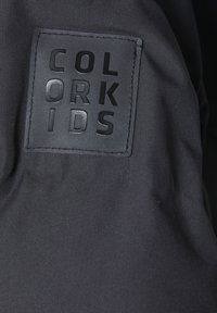 Melnā audumā ir teksturēts, taisnstūris šķērsgriezums ar izspiestu uzrakstu "COLOR KIDS" treknā, lielajā burtiem.