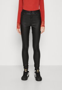 Sorte faux skinnbukser med høy liv høyde, sammen med en rød langermet topp med blonderelastiske mansjetter og svarte sneakers med hvite striper.