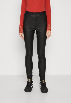 Sorte faux skinnbukser med høy liv høyde, sammen med en rød langermet topp med blonderelastiske mansjetter og svarte sneakers med hvite striper.