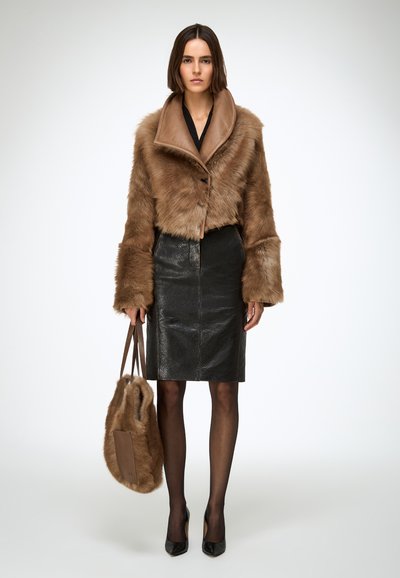 Veste courte en fourrure marron avec un large col, associée à une jupe crayon en cuir noir brillant, des collants noirs transparents et des talons pointus.