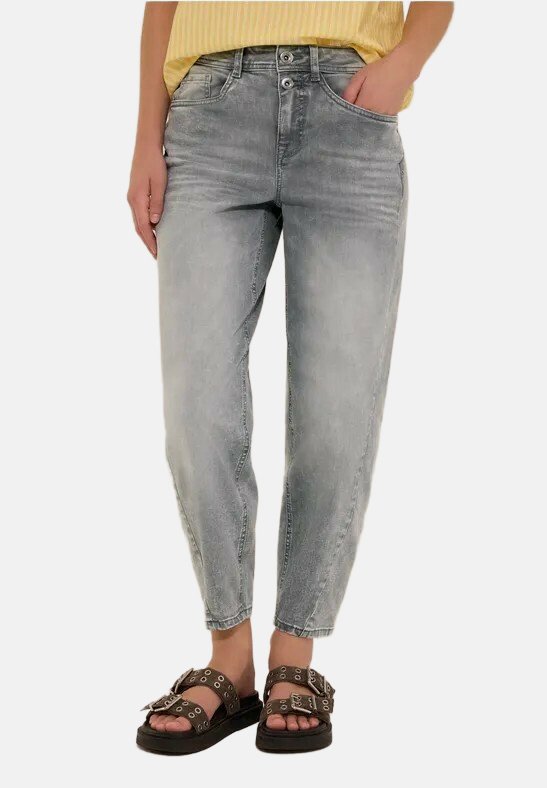 Personne portant un jean gris délavé taille haute avec fermeture à double bouton, une main dans la poche, et des sandales marron à boucle avec semelles épaisses.
