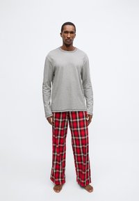 Pelēka krekla ar garām piedurknēm pāris ar sarkaniem pleda pidžamas biksēm. Biksēm ir rakstains raksts ar melniem un krēmkrāsas akcentiem. Ikdienišķa piegriezuma.