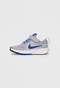 Grijze sportieve schoen met een ademende mesh bovenkant, blauwe accenten, een klittenbandsluiting en een witte middenzool. Beschikt over een gestructureerde rubberen loopzool.