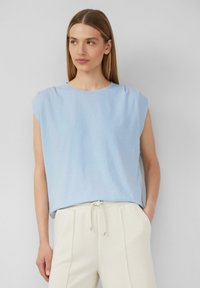 Top azzurro chiaro a maniche corte con una vestibilità morbida, texture delicata e collo rotondo discreto. Abbinato a pantaloni chiari con coulisse.