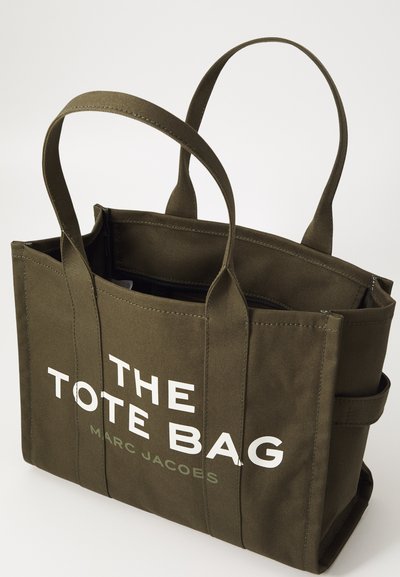 Oliwowa torba płócienna z dwoma uchwytami na ramię, z napisem "THE TOTE BAG" oraz "MARC JACOBS" wydrukowanym dużymi białymi literami.
