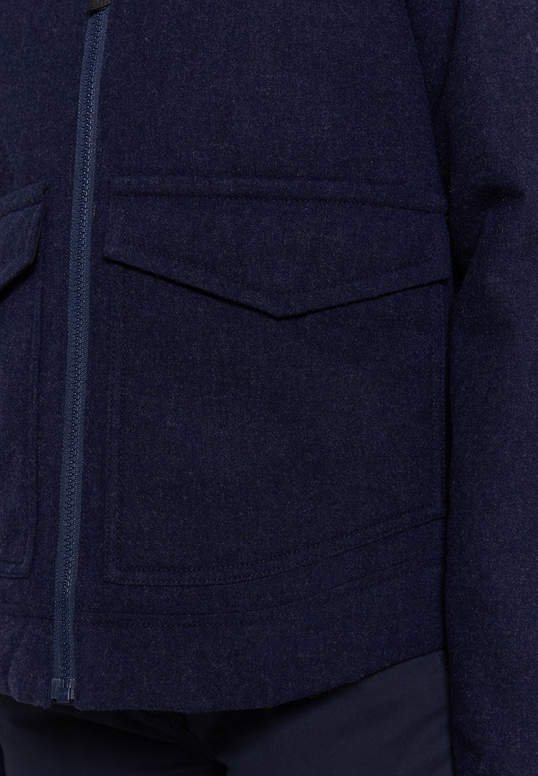 Giacca in lana blu navy con zip frontale, due tasche a pattina e una superficie texturizzata con dettagli cuciti.