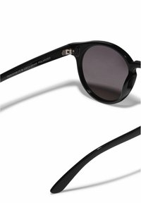 Černé polarizační sluneční brýle s kulatým rámem, tmavě tónovanými skly a hladkým lesklým povrchem; rytí na vnitřní straně spánků.