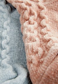 Texturerad tyg i mjuka pastellrosa och blå toner, med upphöjda mönster och en plyschig, mysig yta med en lätt lyster.