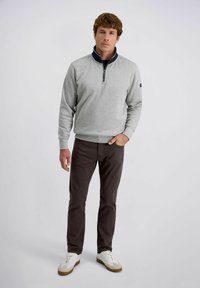 Pull en polaire gris avec col bleu marine, devant zippé quart et poignets côtelés. Associé à un pantalon marron foncé et des baskets blanches.