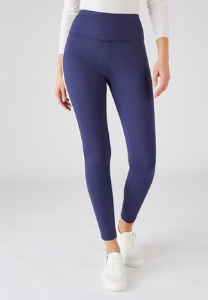 Leggings blu navy realizzati in materiale elasticizzato, con vita alta e dettagli laterali di colore contrastante, abbinati a sneakers bianche.