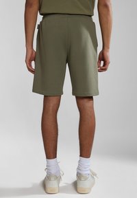 Pantalones cortos de algodón color verde oliva con cintura elástica, de longitud hasta la rodilla, que cuentan con bolsillos laterales y dobladillo doblado, combinados con calcetines y zapatos blancos.