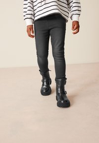 Bottes noires en cuir avec une semelle épaisse, détails de boucle et zips. Portées avec un jean foncé et un haut rayé blanc. Texture lisse.
