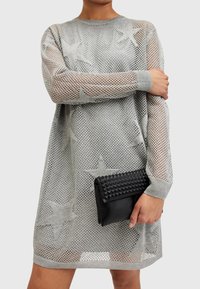 Sølvmesh-kjole med stjernesymboler, lange ermer og ribbede mansjetter. Kombinert med en teksturert svart clutch-veske med høye nagler.
