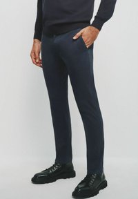 Granatowe, wąskie spodnie uszyte z gładkiego materiału, z kieszeniami z przodu, noszone z czarnymi sznurowanymi botkami na masywnych podeszwach.