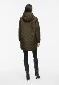 Parka matelassée verte olive avec un design à dos plus long. Présente une texture lisse, des manches larges et un ourlet arrondi.