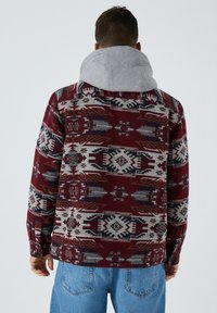 Rød og grå mønstret skjorte med geometriske designs, der har en grå hætte, knaplukke ved ærmerne og en afslappet pasform, lavet af struktureret stof.