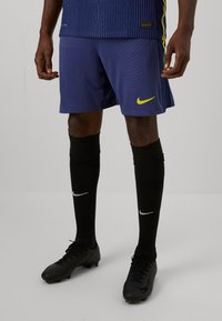 Marineblauwe Nike-shorts met gestructureerde strepen, gecombineerd met kniehoge zwarte sokken met het witte Nike-logo en zwarte voetbalschoenen.