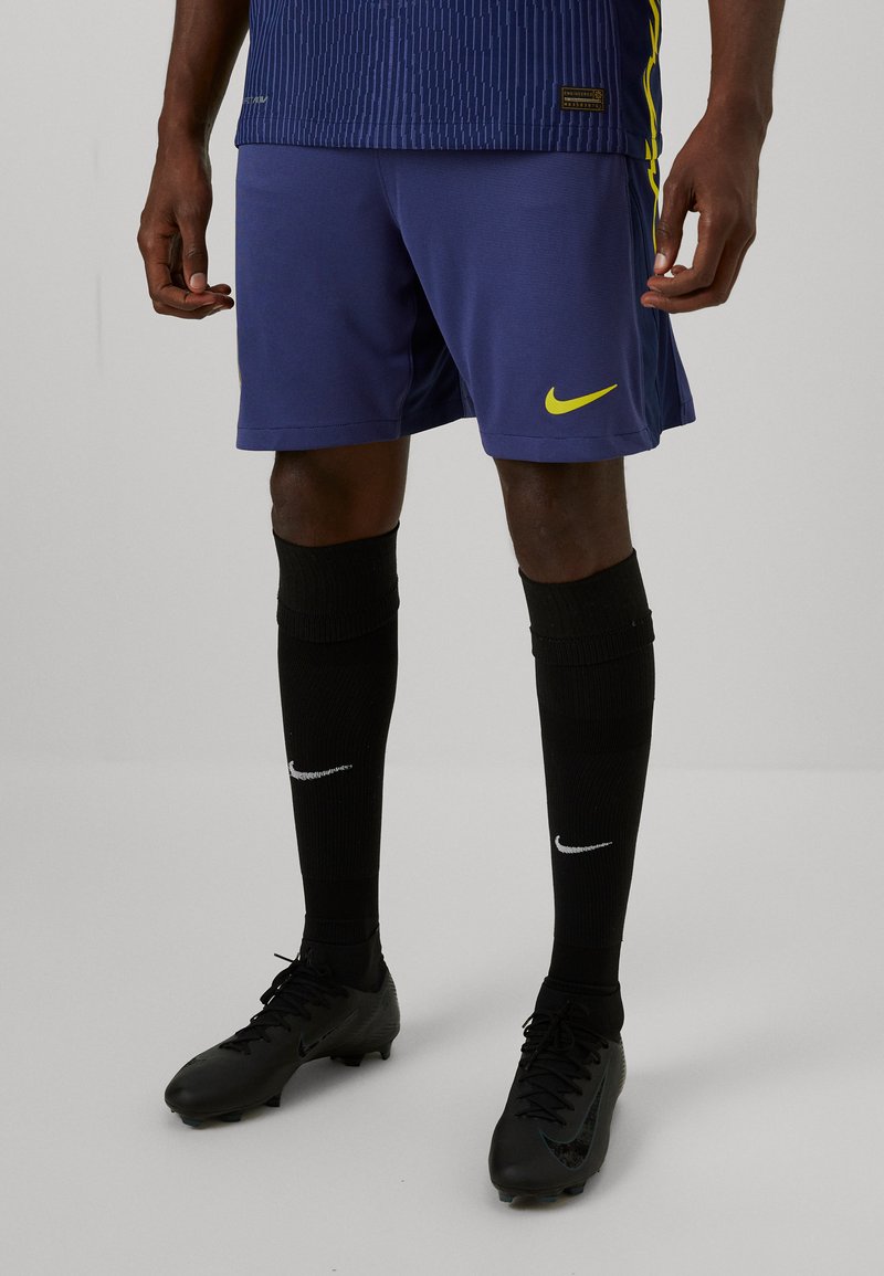 Navyblaue Nike-Shorts mit strukturierten Streifen, kombiniert mit knielangen schwarzen Socken mit weißem Nike-Logo und schwarzen Football-Stiefeln.