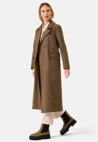 Bruine wolmix jas met een notched lapel, enkele knoopsluiting, zijzakken en een lange silhouet. Gecombineerd met olijfgroene enkellaarsjes.